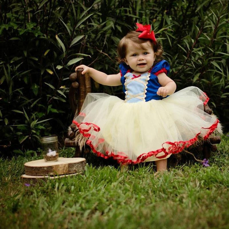 Child in Snow White costume sitting outdoors on a grassy area with greenery.