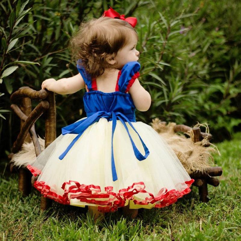 Child in a Snow White costume standing outdoors with greenery in the background