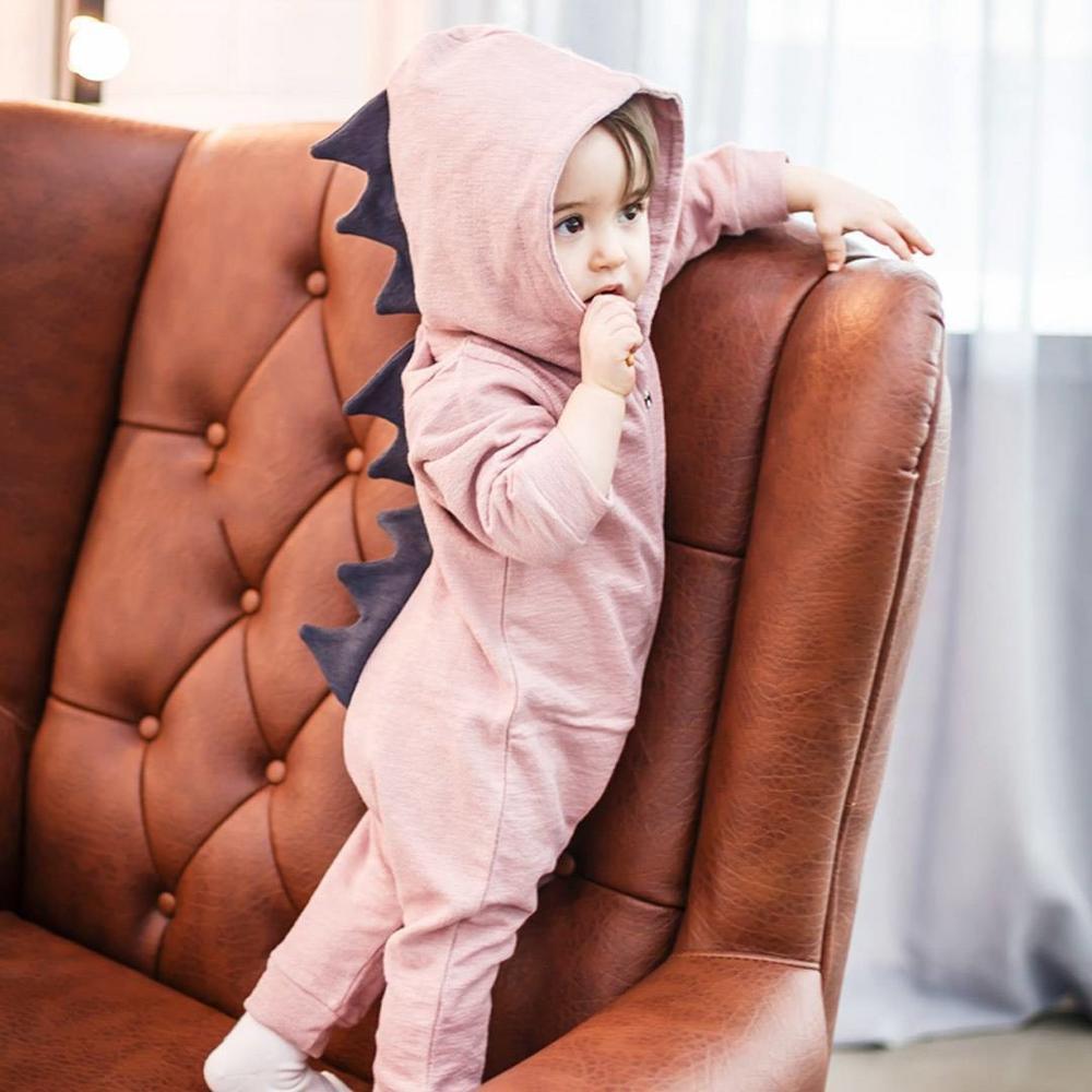 Child in a pink dinosaur onesie sitting on a brown leather chair.