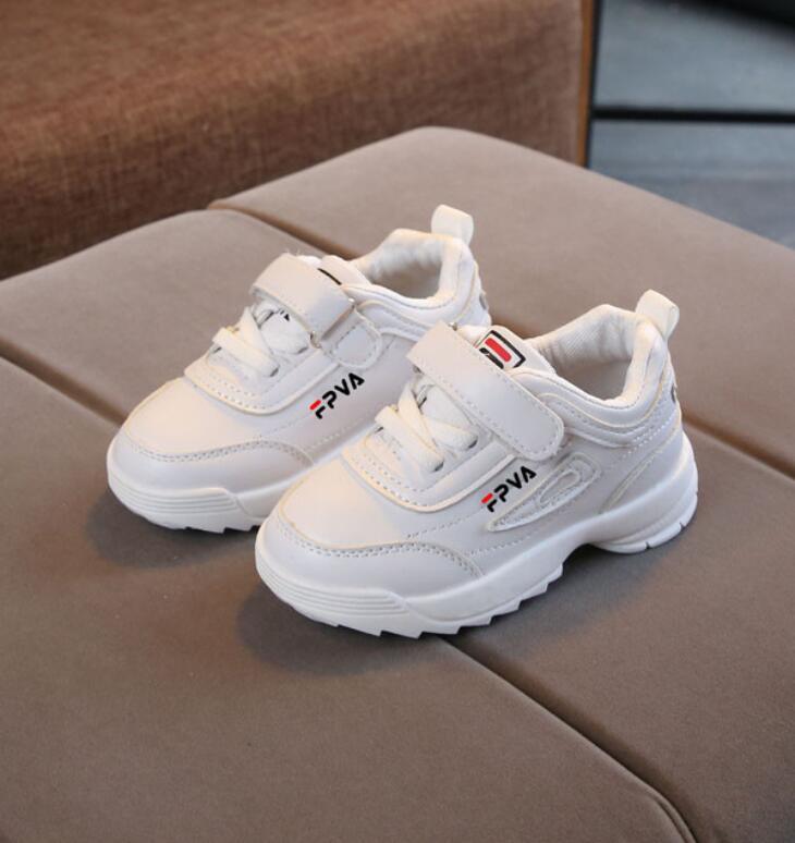 White children's sneakers with visible branding on a brown surface