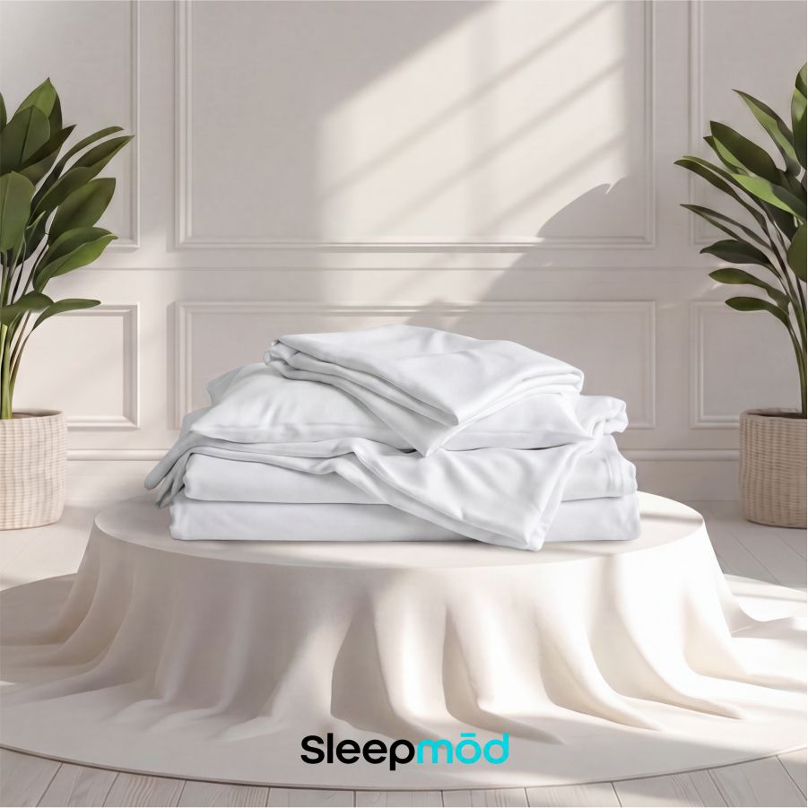 Stack of white bedding on a bed with 'Sleepmod' branding in a bright room.