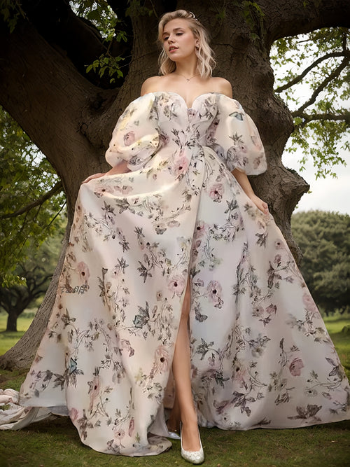 Woman in a floral dress standing in a park-like setting with trees and greenery.
