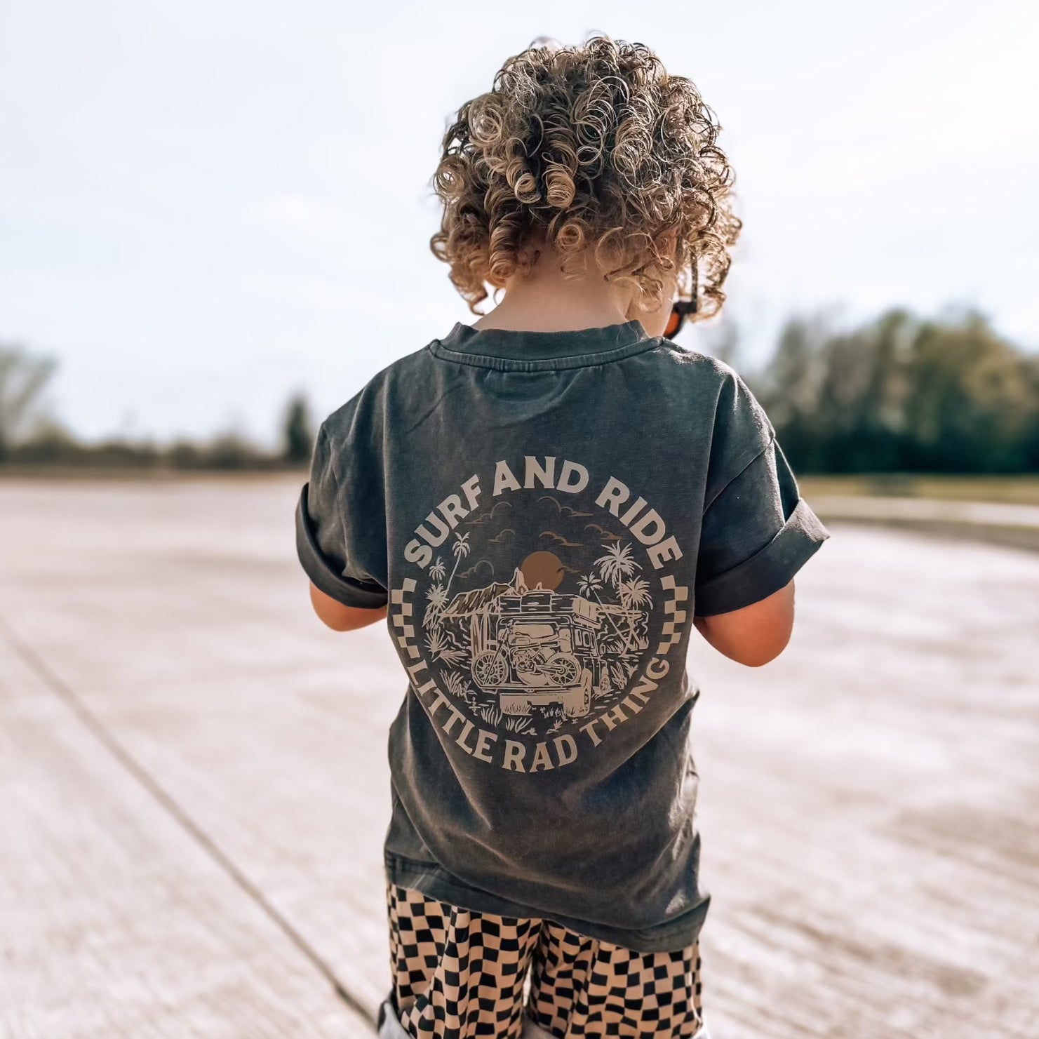 Child wearing a shirt with 'Surf and Ride' design outdoors