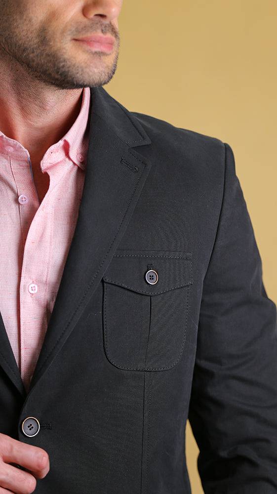 Man wearing a black blazer over a pink shirt against a beige background