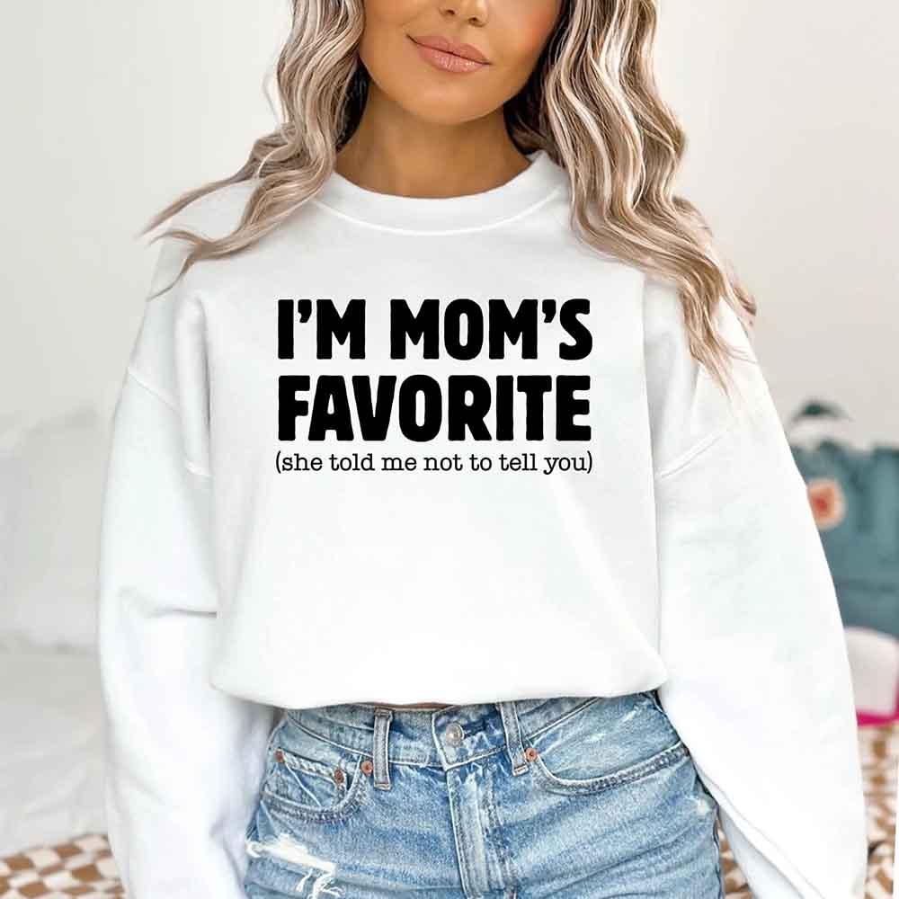 Person wearing a white sweatshirt with text 'I'M MOM'S FAVORITE (she told me not to tell you)'