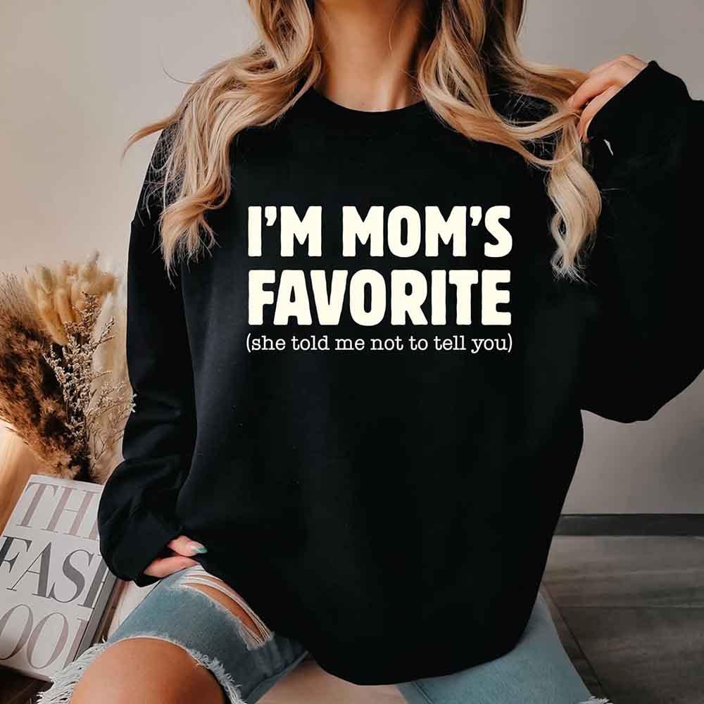Person wearing a black sweatshirt with 'I'm Mom's Favorite (she told me not to tell you)' text.
