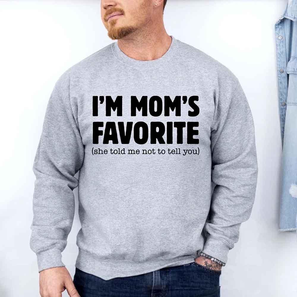 Person wearing a gray sweatshirt with text 'I'm Mom's Favorite (she told me not to tell you)' on a white background
