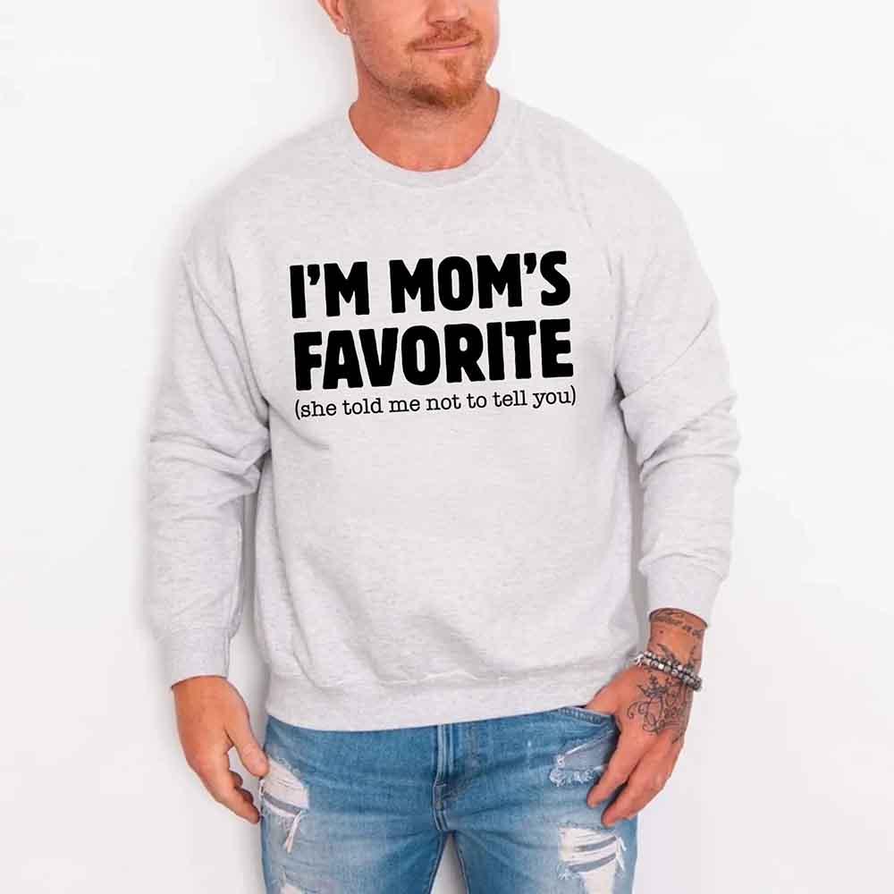 Person wearing a gray sweatshirt with text 'I'M MOM'S FAVORITE (she told me not to tell you)' on a white background