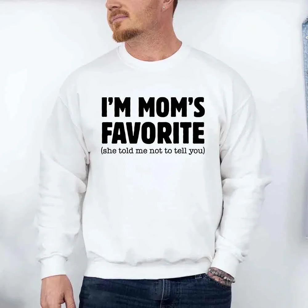 Person wearing a white sweatshirt with text 'I'M MOM'S FAVORITE (she told me not to tell you)' on a plain background