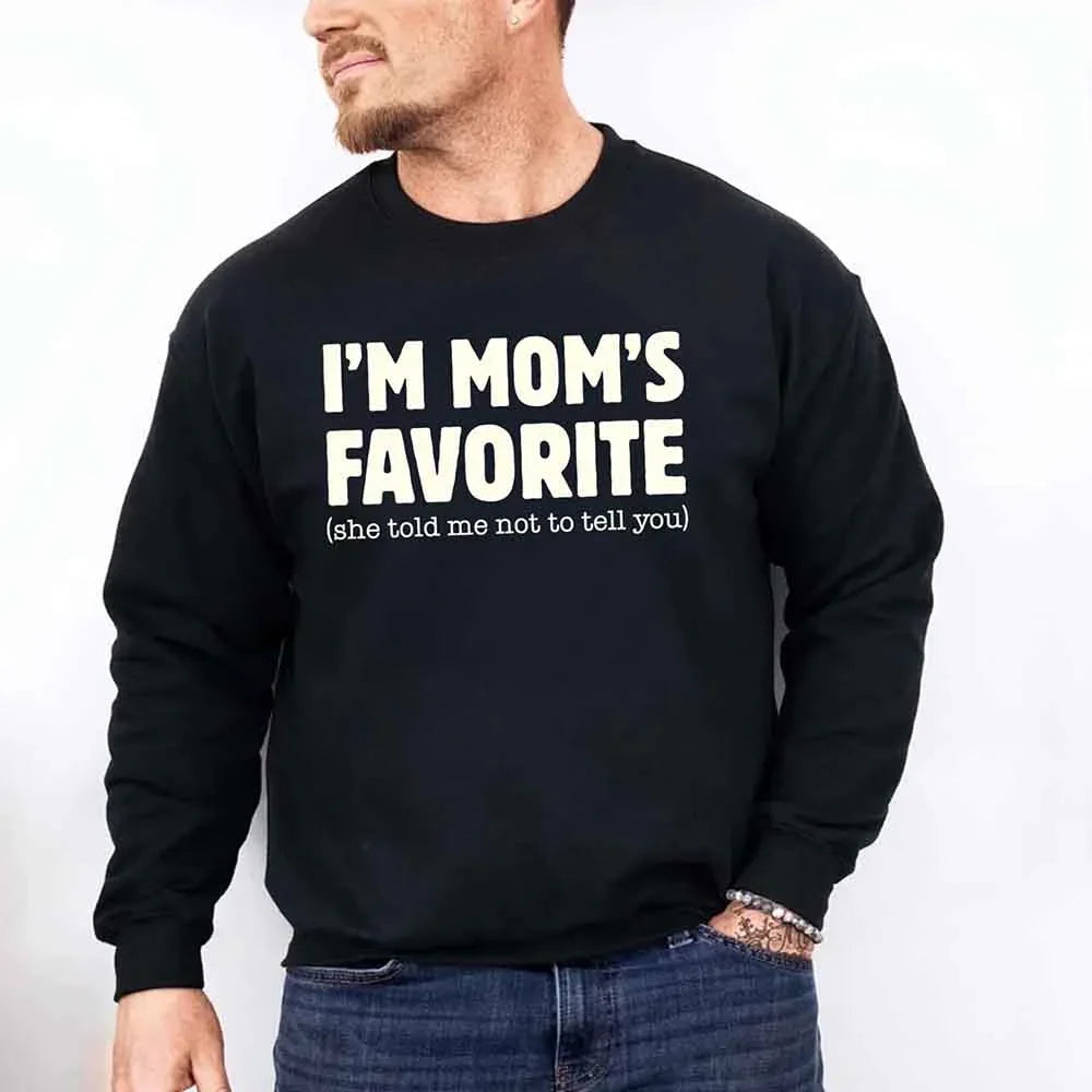 Person wearing a black sweatshirt with text 'I'M MOM'S FAVORITE (she told me not to tell you)' on a plain background