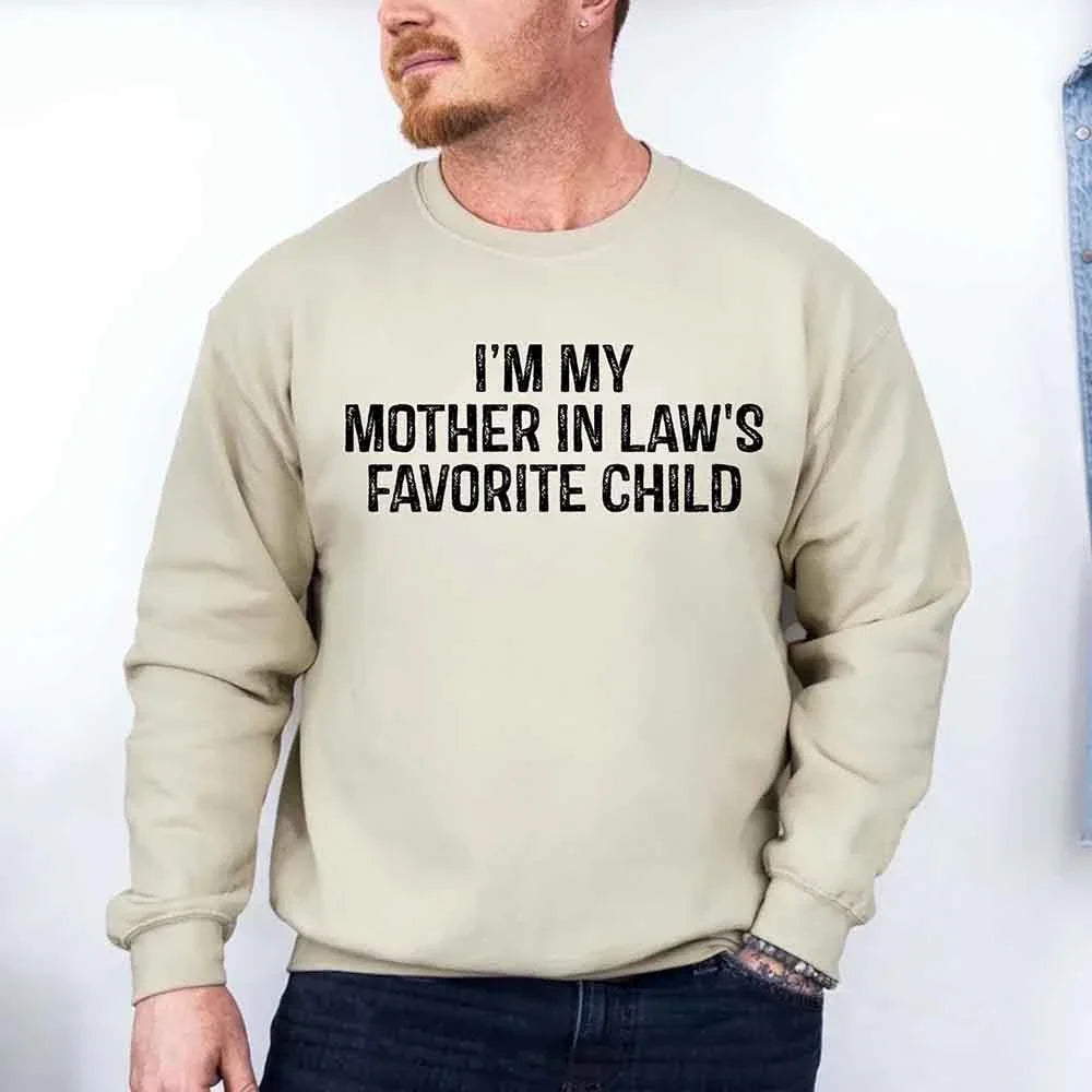 Man wearing a beige sweatshirt with text 'I'm my mother in law's favorite child' on a plain background
