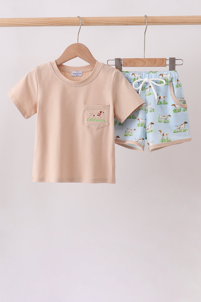 Children's beige t-shirt and blue shorts with dog pattern on a wooden hanger against a light gray background