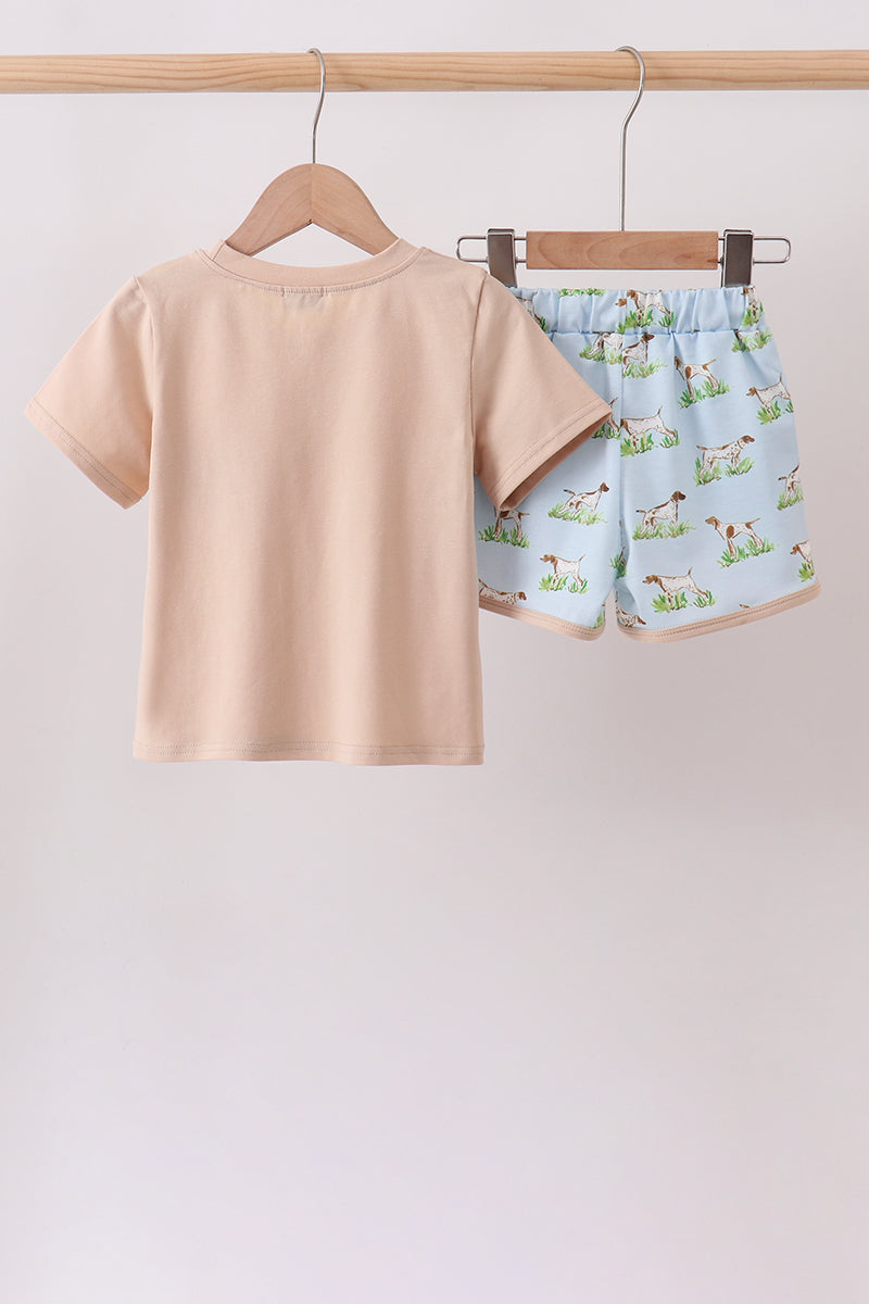 Children's beige t-shirt and patterned shorts hanging on a rack against a light background