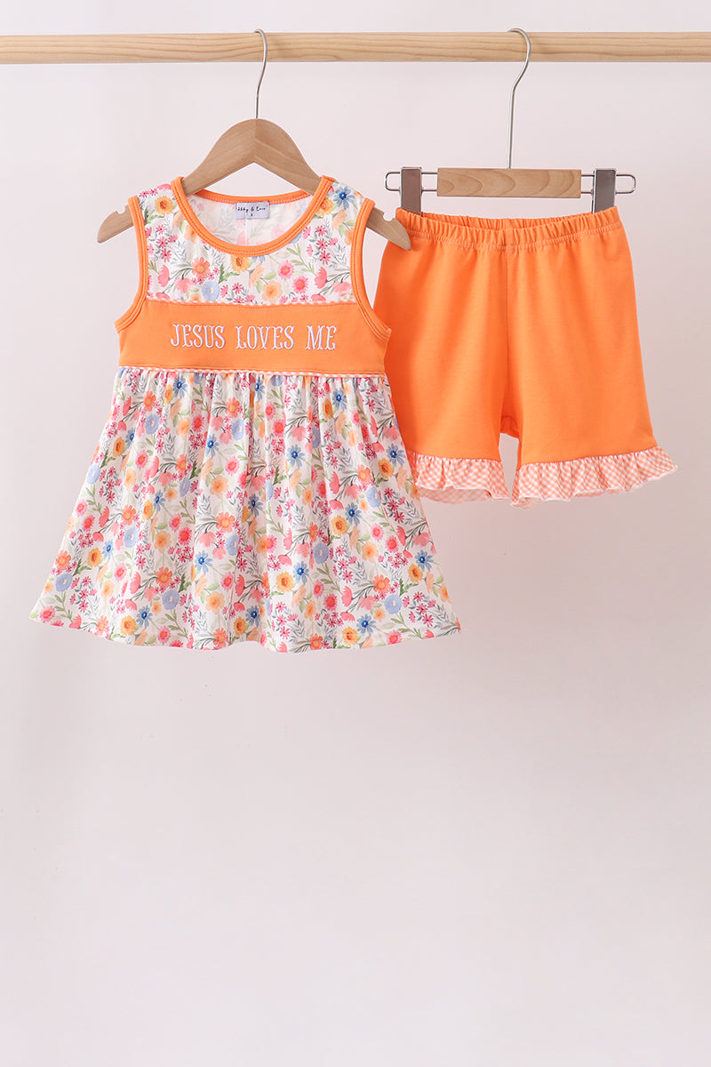 Children's outfit with floral dress and orange shorts on hangers against a white background