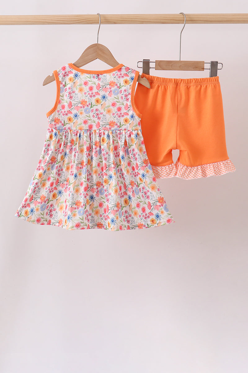 Children's floral dress and orange shorts set on hangers against a white background