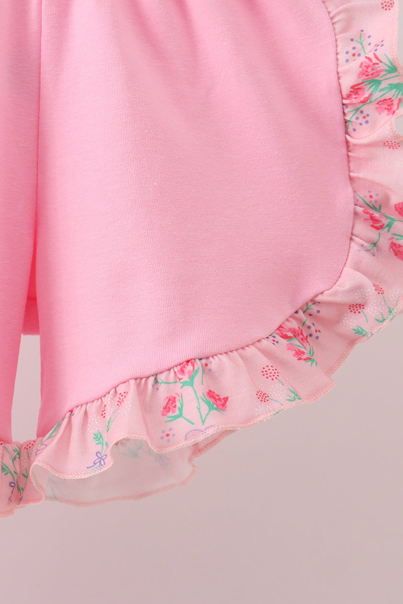 Close-up of a pink garment with floral ruffle trim on a light gray background