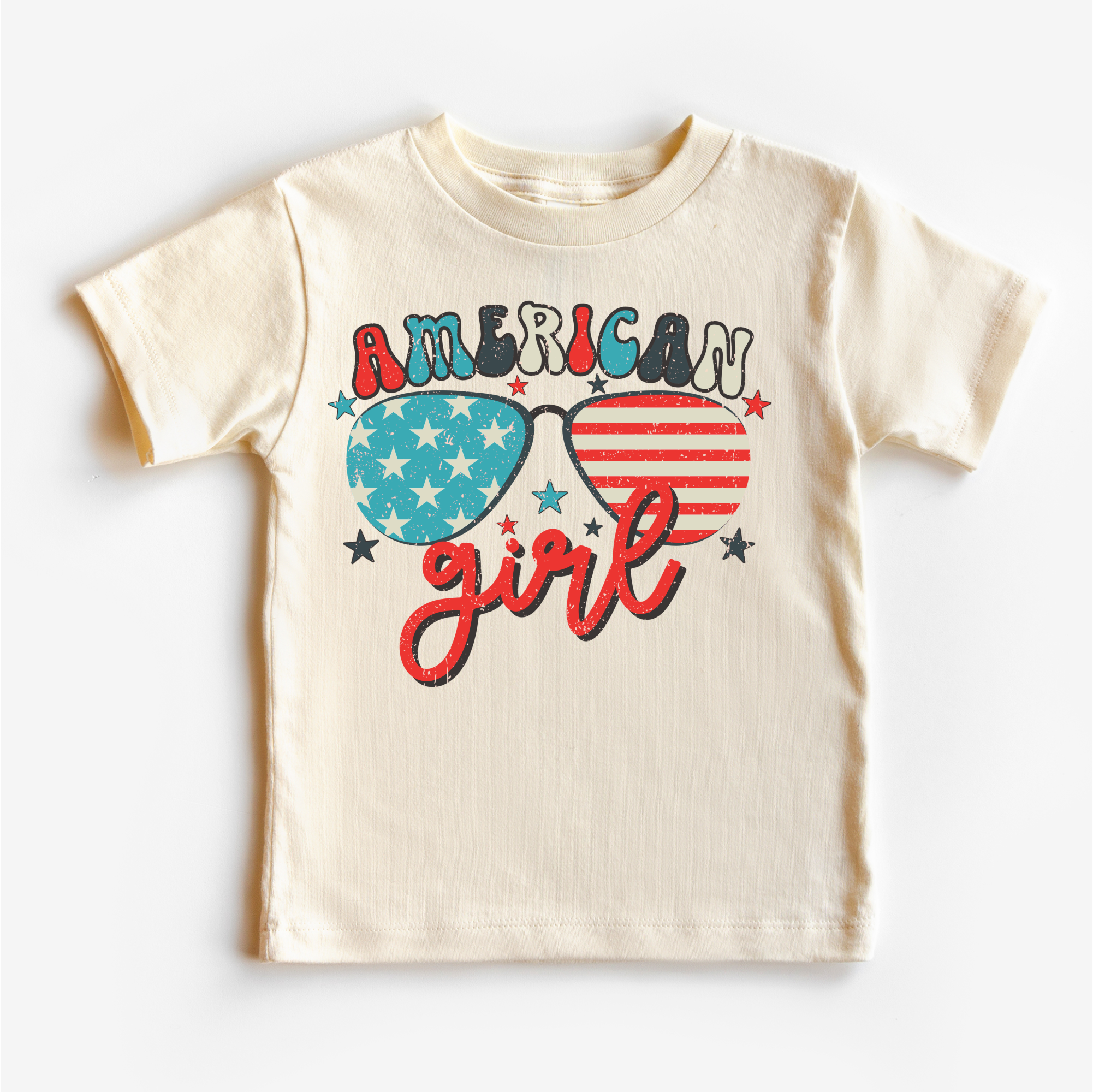 Beige t-shirt with 'American Girl' design featuring sunglasses with American flag and star patterns on a white background.
