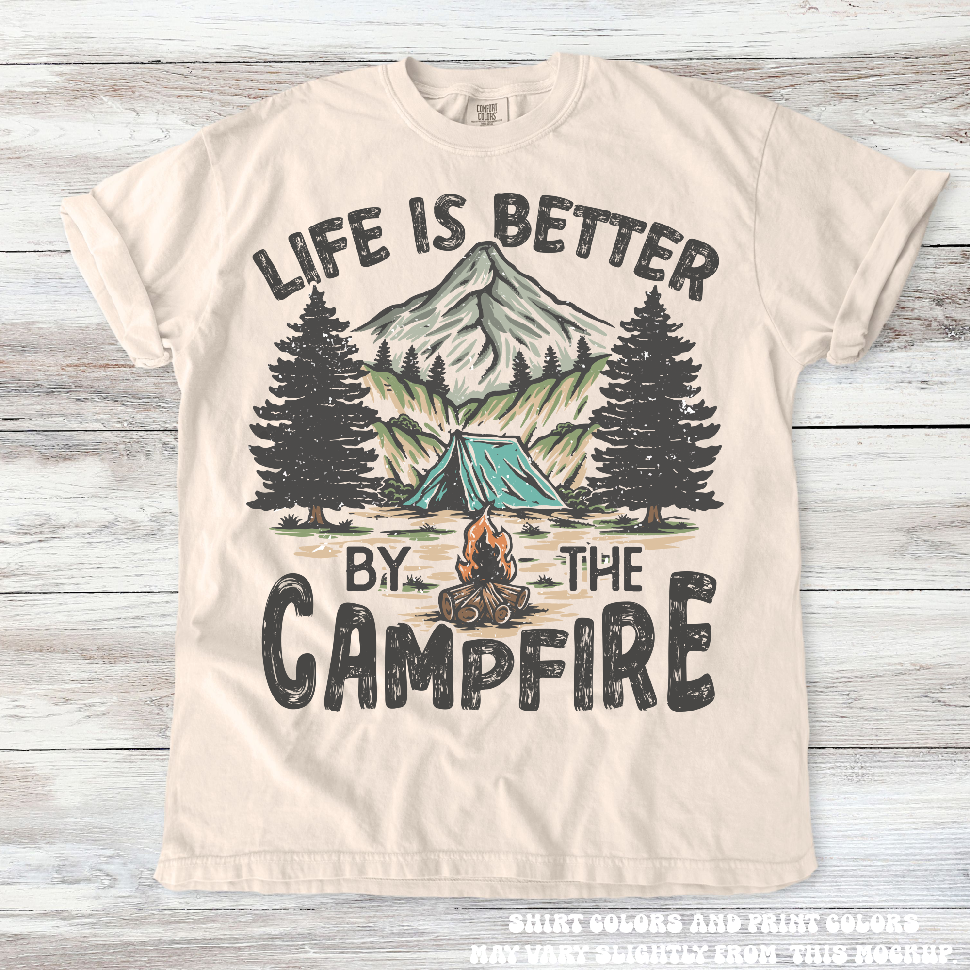 Beige t-shirt with 'Life is Better by the Campfire' graphic on a wooden background