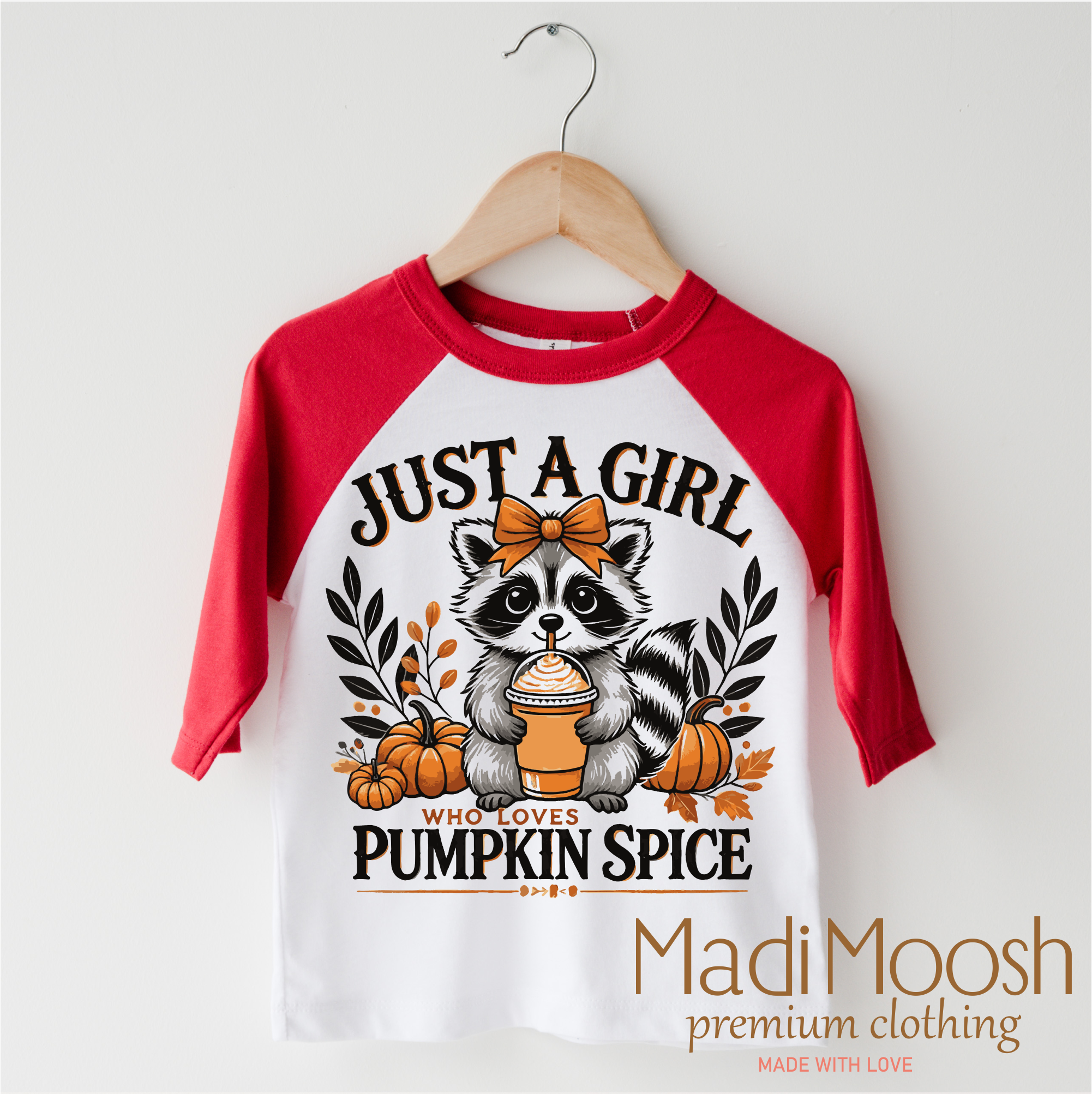 Children's 3/4 sleeve shirt with raccoon graphic and text 'Just a girl who loves pumpkin spice' by Madi Moosh on a hanger.