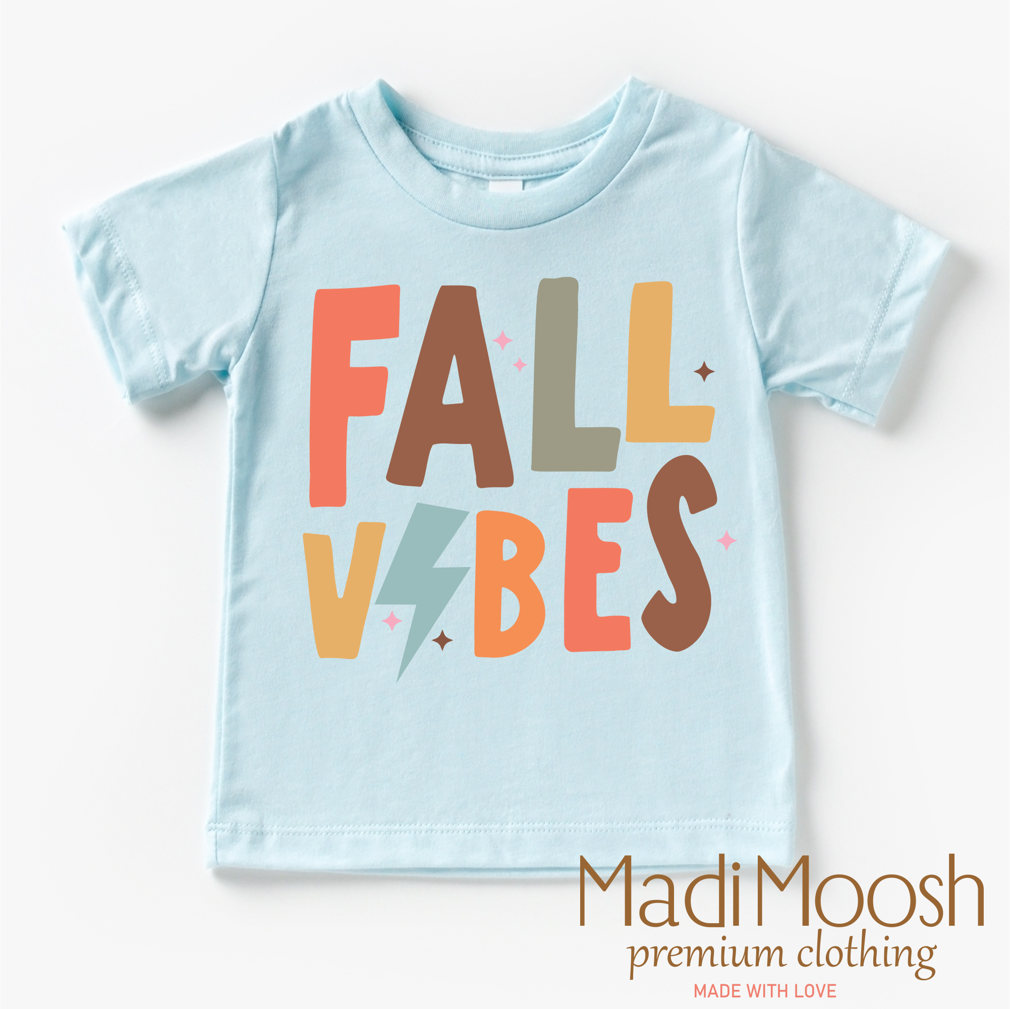 Light blue t-shirt with 'FALL VIBES' text in colorful letters on a white background, branded with Madi Moosh.