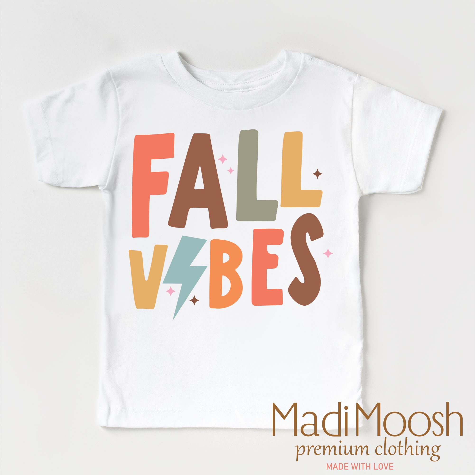 White t-shirt with 'FALL VIBES' text in colorful letters on a white background, featuring the brand 'Madi Moosh'.