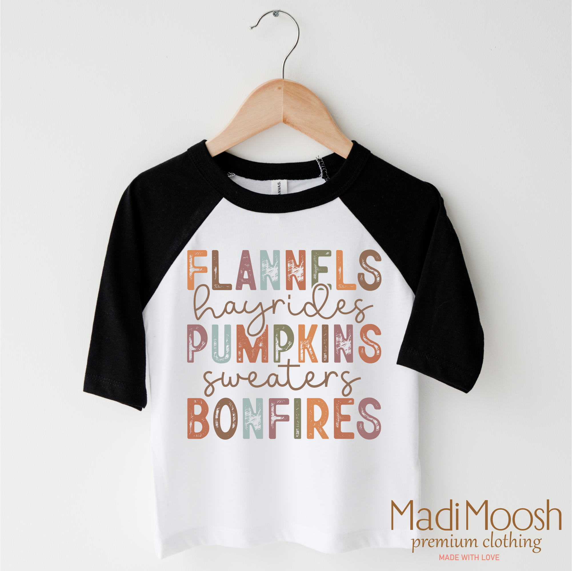 Children's black and white 3/4 sleeve raglan shirt with autumn-themed text on a hanger against a white background.