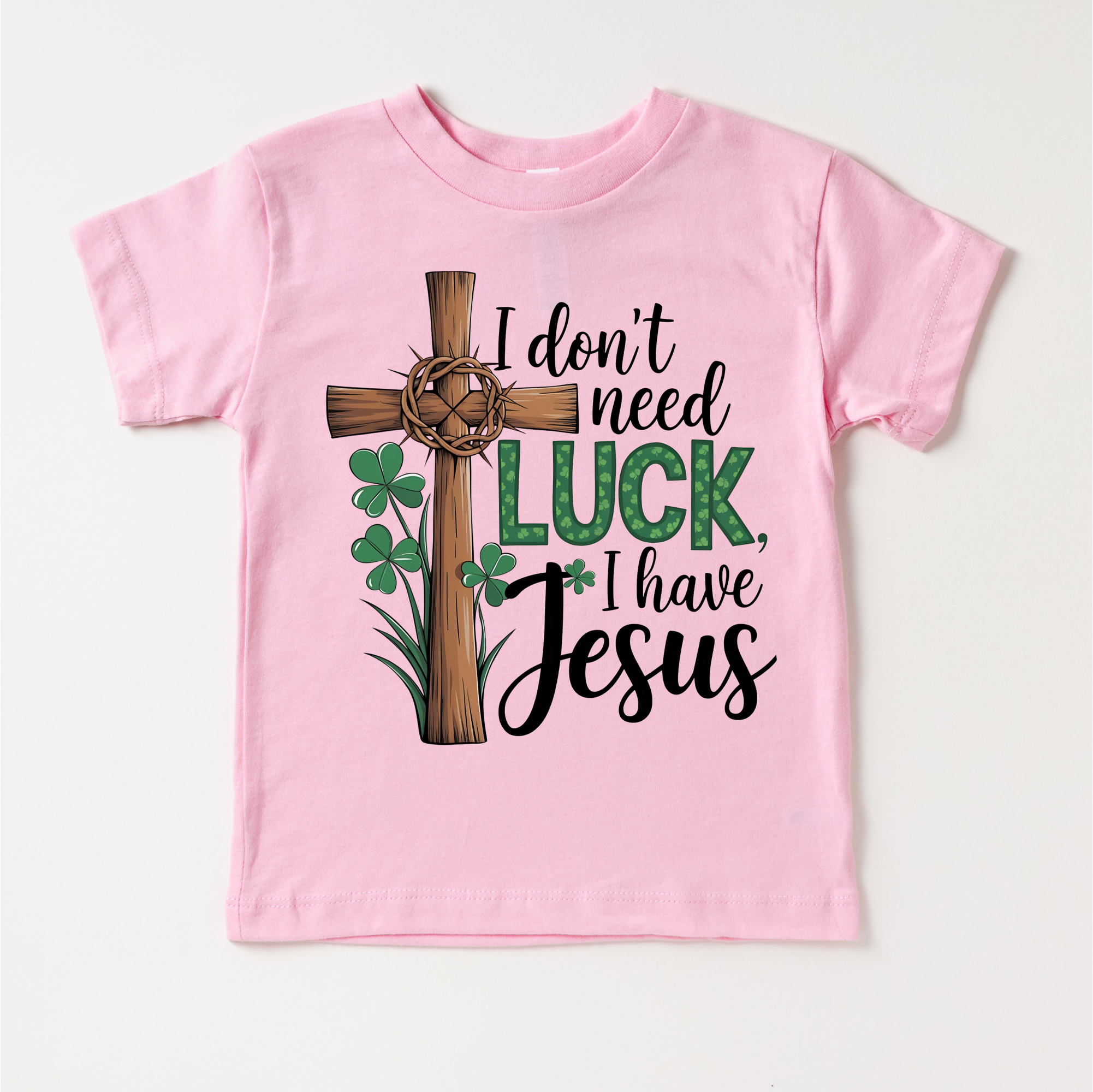 Pink t-shirt with a cross, shamrocks, and text 'I don't need luck, I have Jesus' on a white background