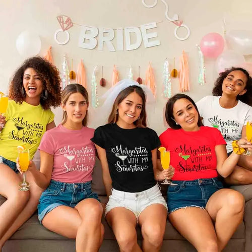 Five women sitting on a couch wearing matching t-shirts with a bridal party theme, surrounded by balloons and decorations.