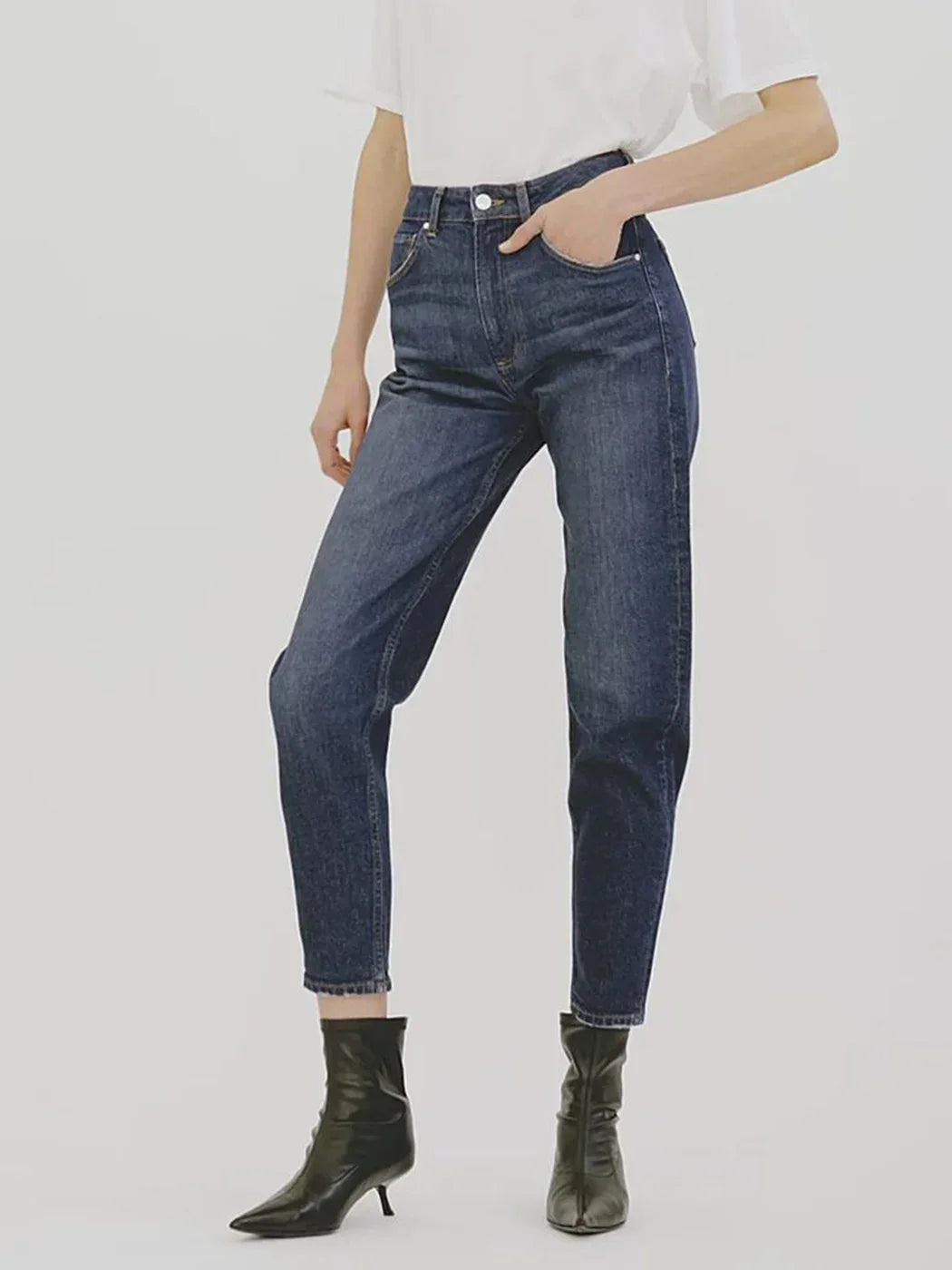 Person wearing blue jeans and black boots on a white background