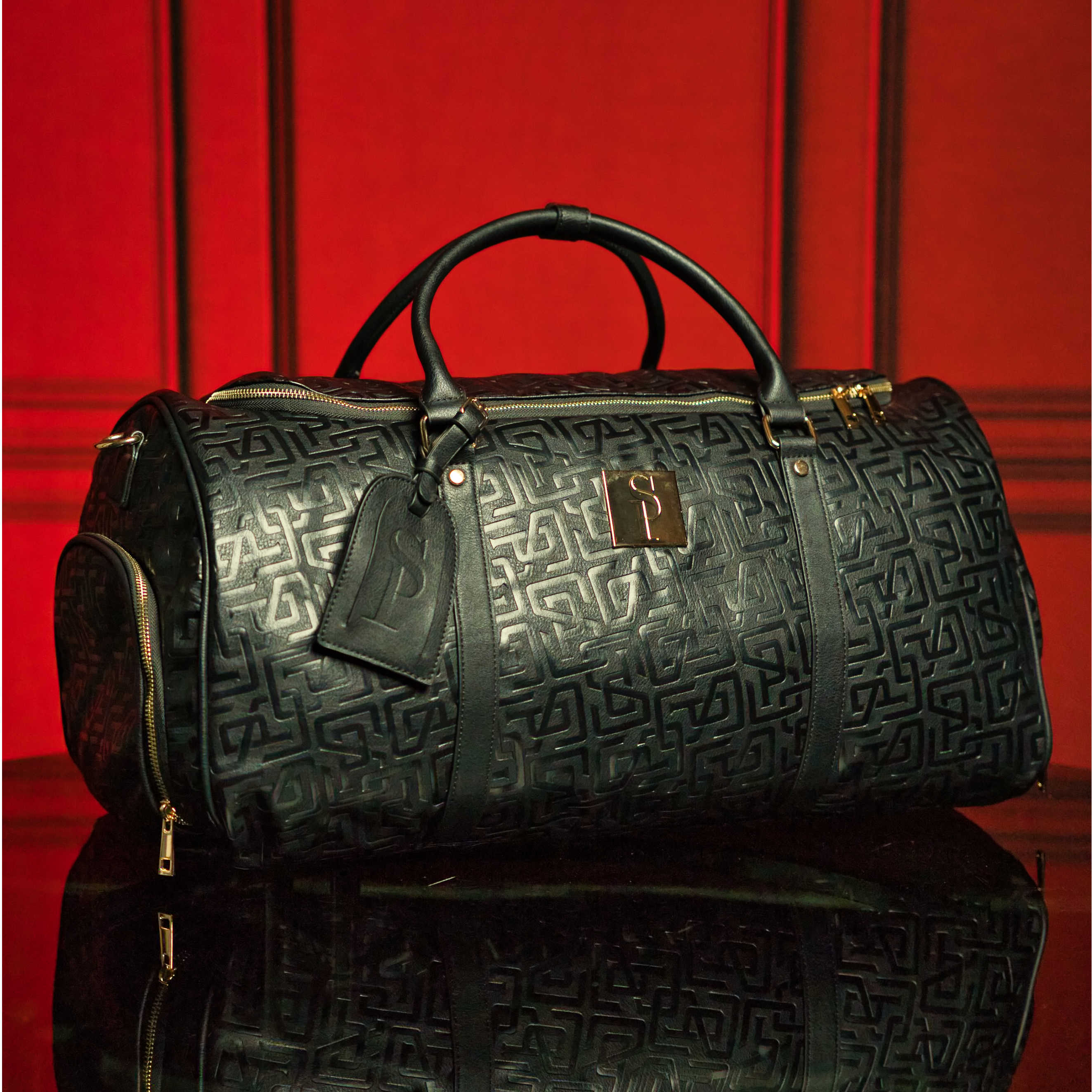 Black textured duffel bag with gold accents on a red background