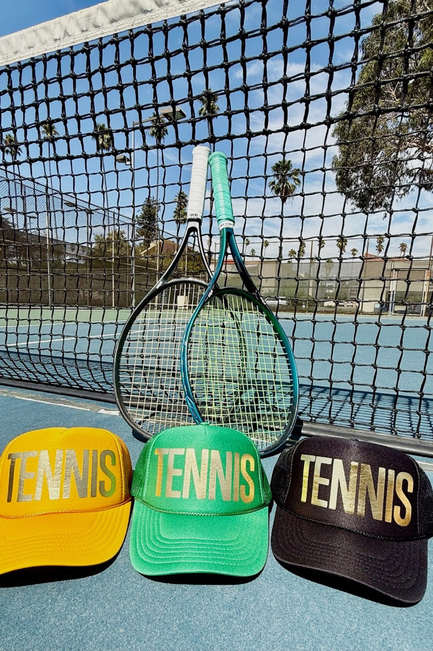 Three tennis-themed hats on a tennis court with a racket and net in the background.