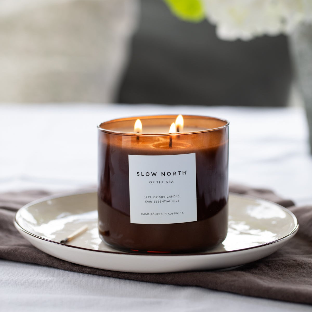 Candle with a label on a white plate, sitting on a surface with a blurred background