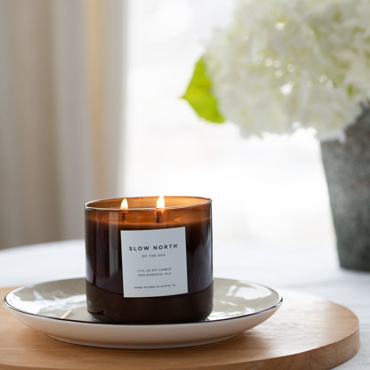 Candle labeled 'Slow North' on a white plate with a blurred background