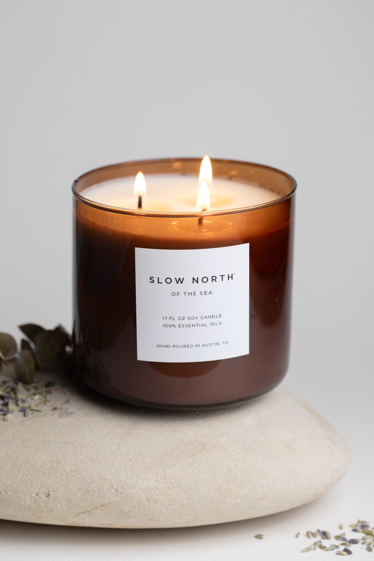 Lit candle in a brown glass jar with a label on a light gray background