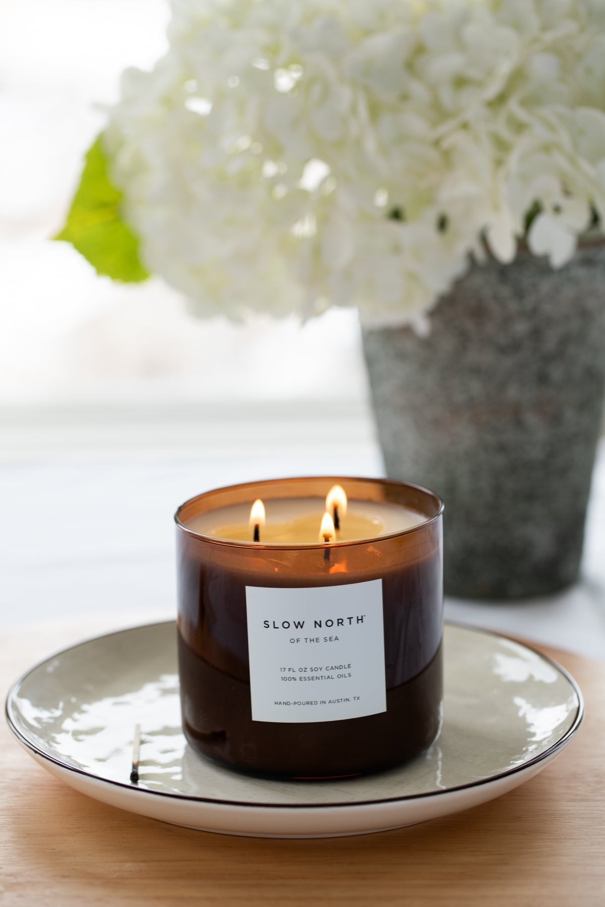 Candle with a label on a plate, with flowers in the background