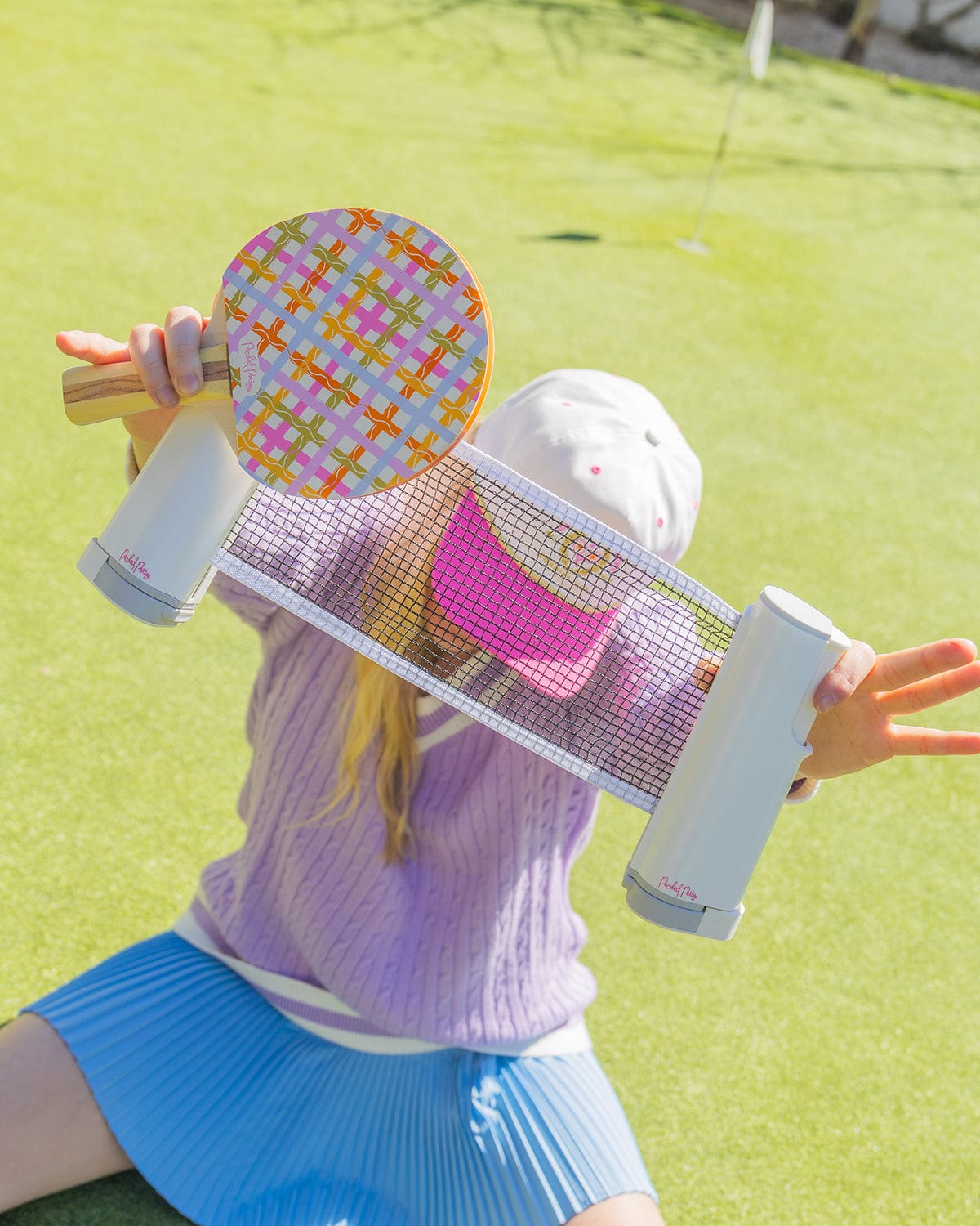 Person holding a colorful paddle and tennis racket on a green court