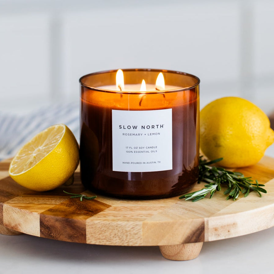 Candle with 'Slow North' label on a wooden board with lemons and rosemary
