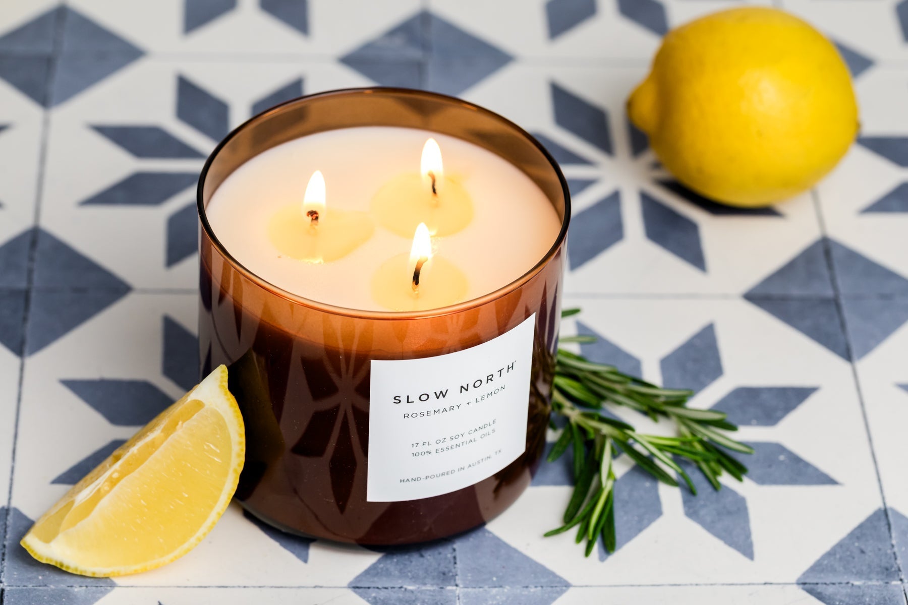 Candle with 'Slow North' label on a decorative tile background with lemons and rosemary.