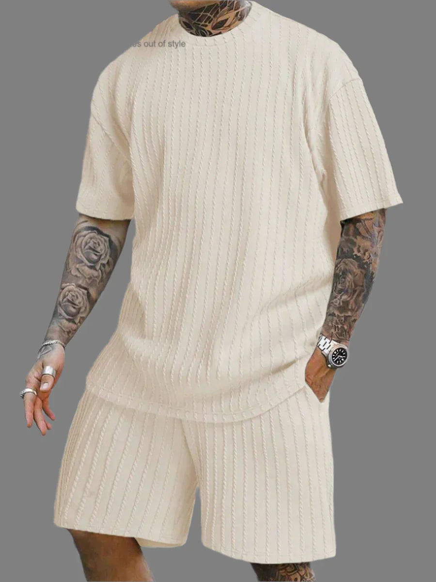 Person wearing a beige ribbed knit outfit with tattoos on arms and a watch on wrist.