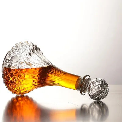 Glass decanter with a textured base and clear top, filled with amber liquid on a reflective surface.