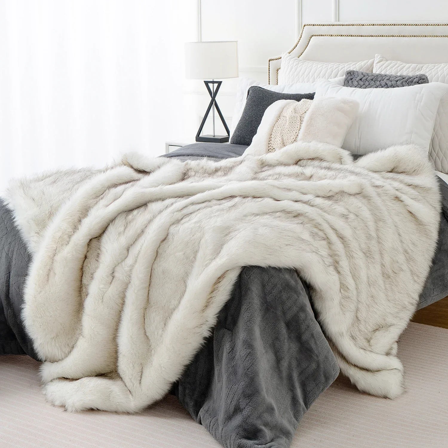 White and gray fluffy blanket draped over a bed in a bedroom setting.