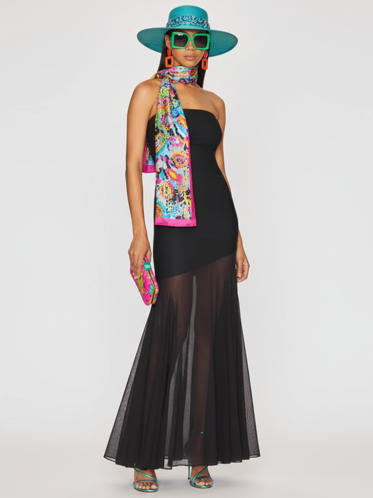 Woman wearing a black dress with sheer overlay, colorful scarf, and turquoise hat on a white background