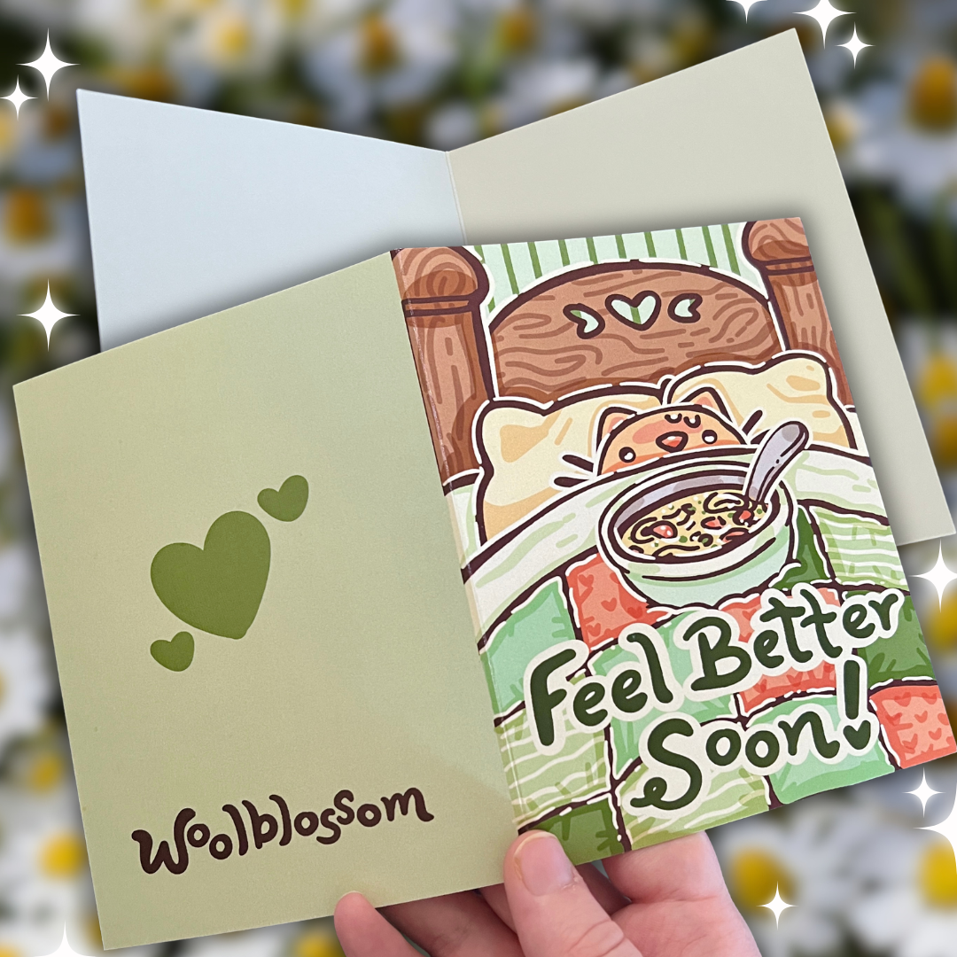 Greeting card with cartoon cat in bed and 'Feel Better Soon!' text, held open by a hand.