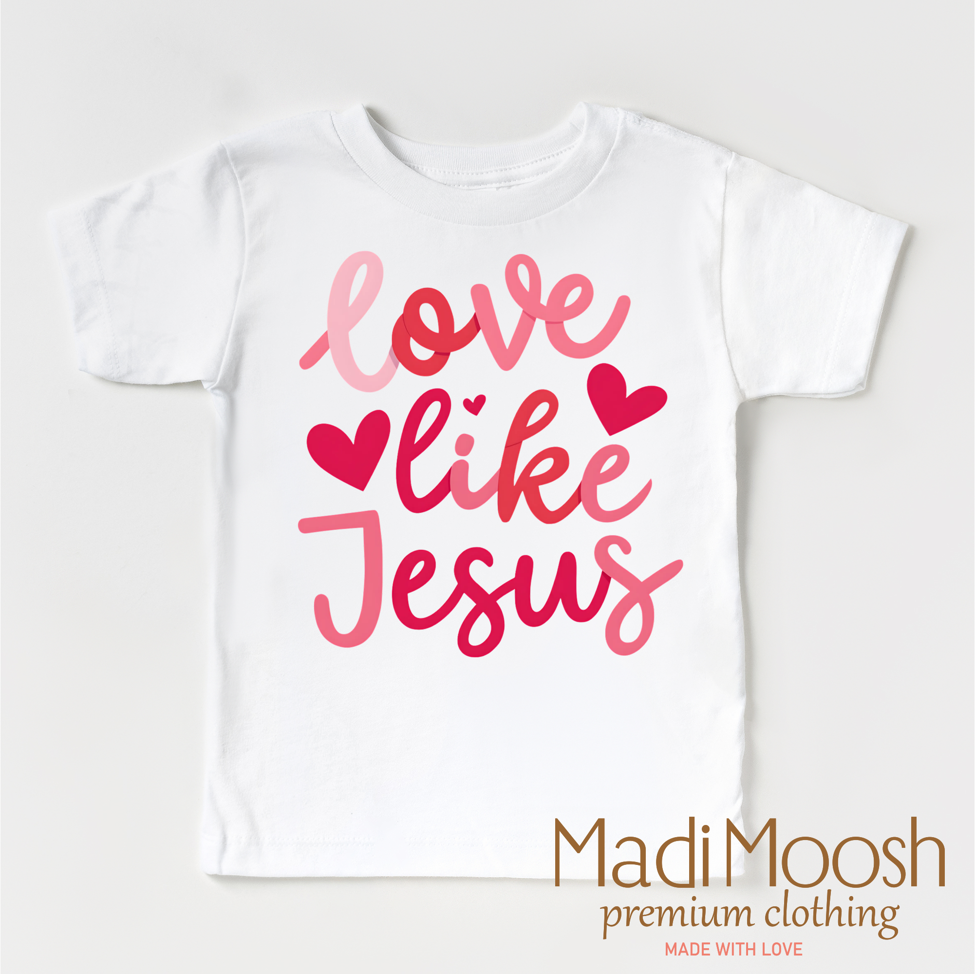 White t-shirt with 'Love like Jesus' text in pink on a white background, featuring the brand 'Madi Moosh'.