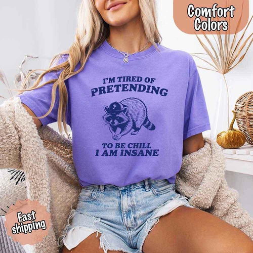 Person wearing a purple t-shirt with a raccoon graphic and text, sitting on a couch.