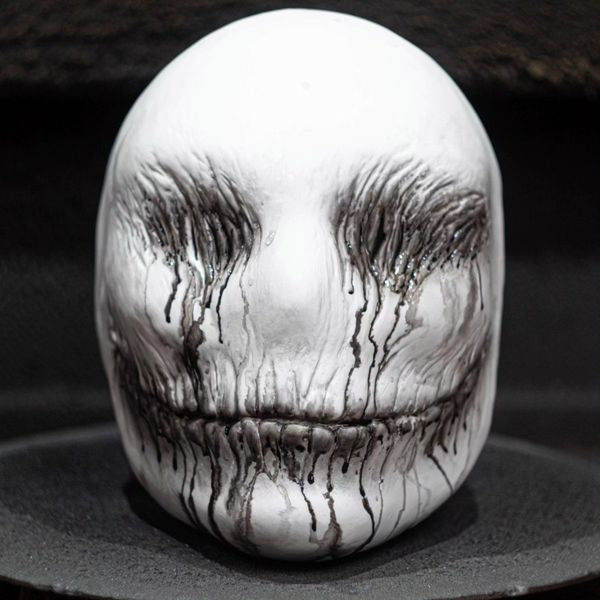 Silver skull-shaped object with engraved facial features on a dark background
