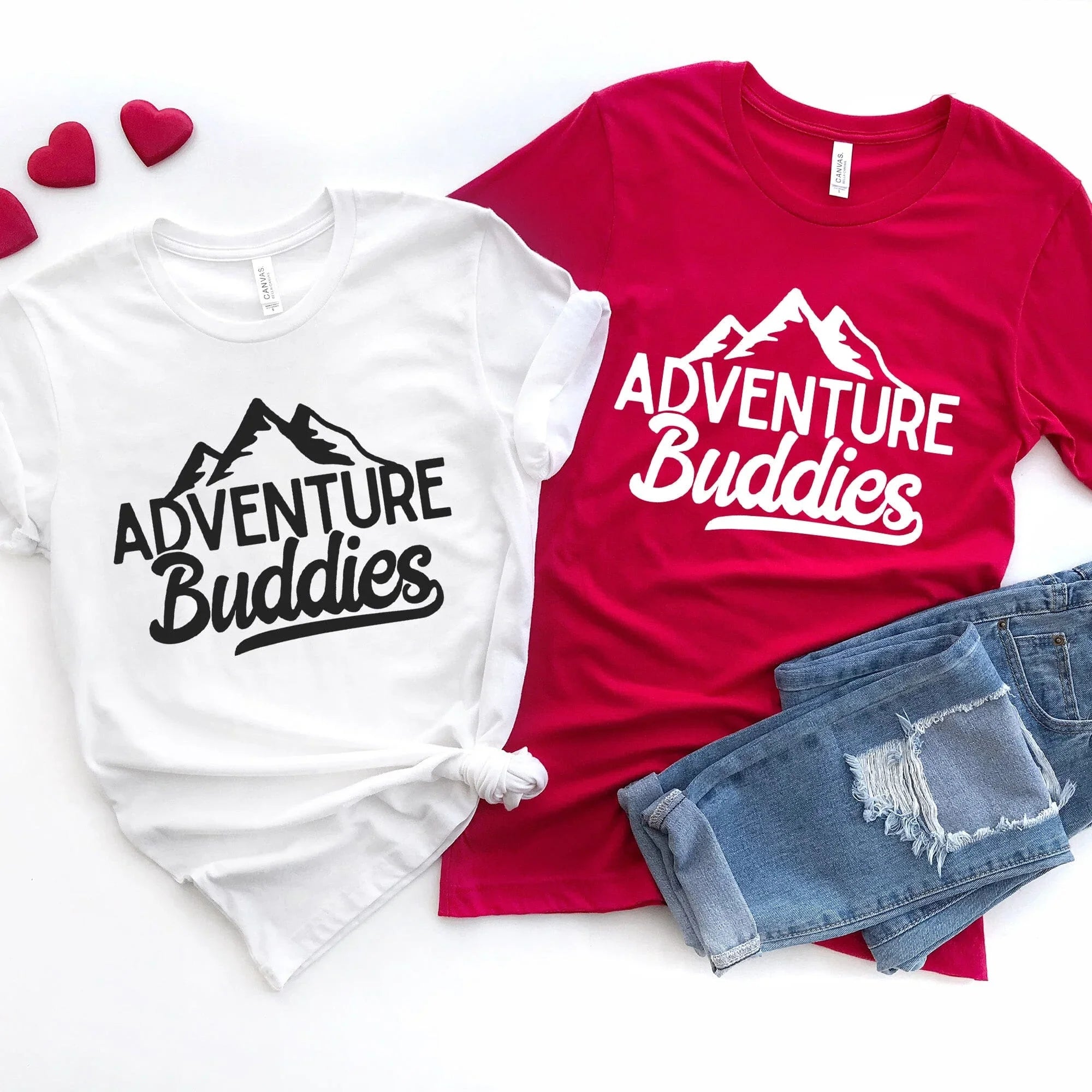 Two t-shirts with 'Adventure Buddies' text and mountain graphics, paired with denim shorts on a white background.