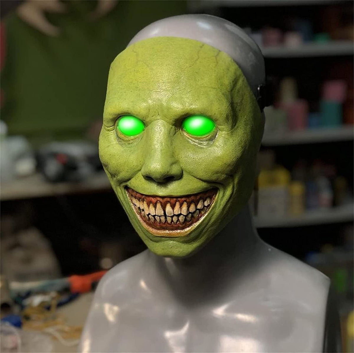 Green mask with glowing eyes on a mannequin head against a blurred background