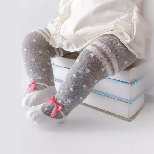 Child wearing gray tights with white polka dots and pink bows on a light background