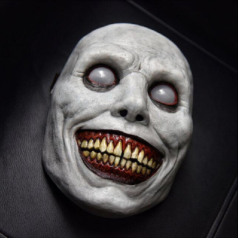 Horror-themed mask with white face, red eyes, and open mouth showing teeth on a dark background.